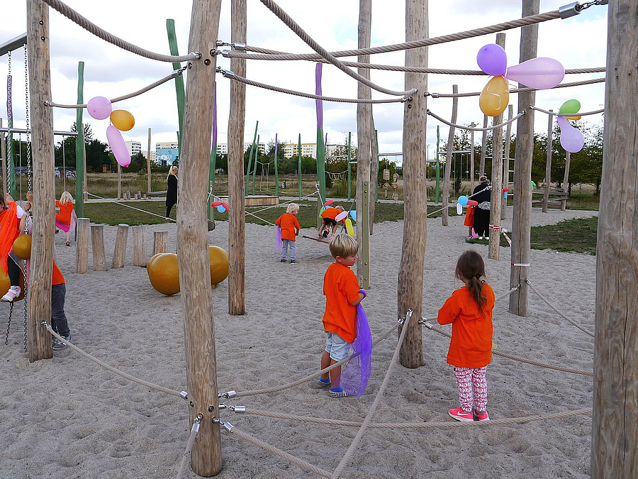 Kinder im Balancierparcours aus Holzstangen und Seilen mit Luftballons