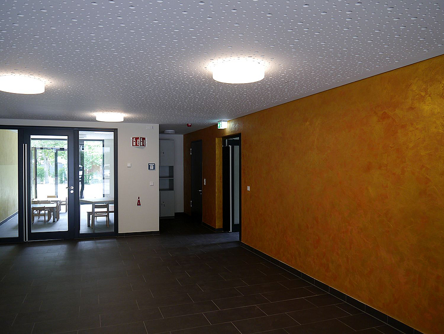 Niedriges Foyer mit dunkelgelber Wand, helle Schallschutzdecke