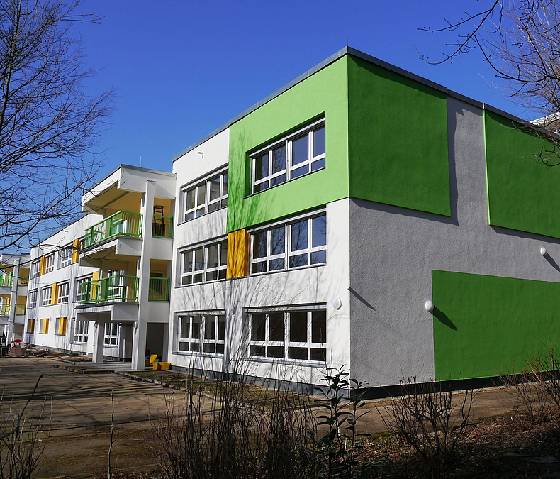 Rückwärtige Fassade einer sanierten Typenbau-Kita mit grünen und gelben Akzenten