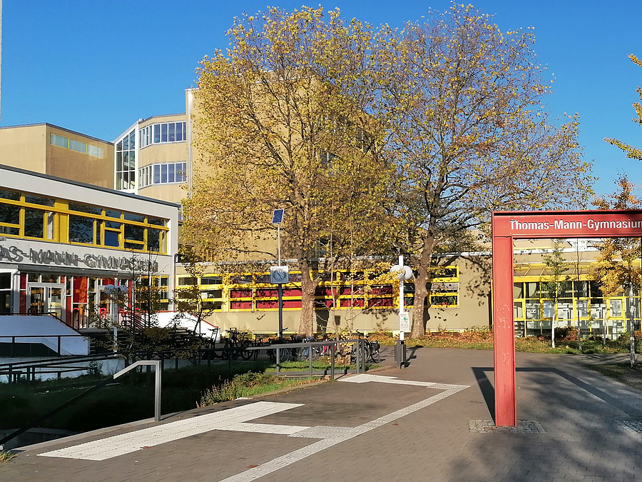 Platz mit Leitstreifen, Schulgebäude, Rotes, stilisiertes Metalltor, Bäume