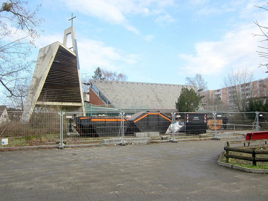 Modernes Kirchengebäude, davor Bauzaun
