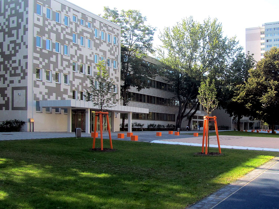 Schulgebäude mit Digitalmuster an der Fassade, Rasen, junge Bäume