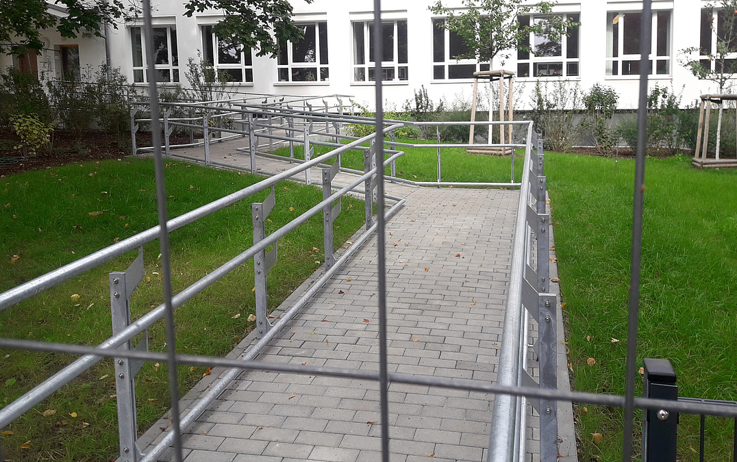 Rampe mit Geländer durch Rasen zu Schulgebäude