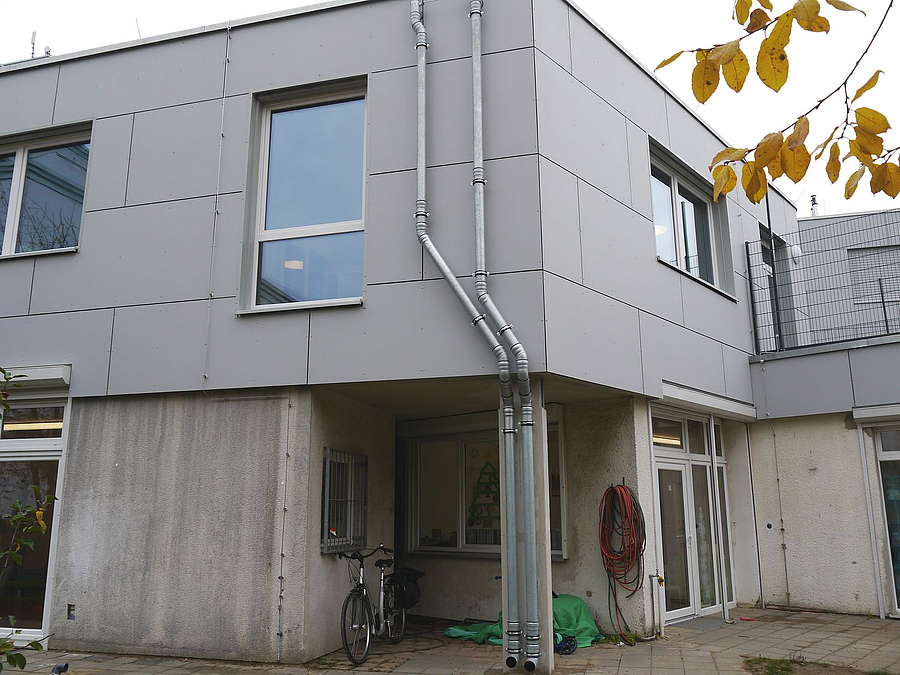 Zweigeschossige Gebäudeecke, oben mit grauen Platten verkleidet, unten Beton