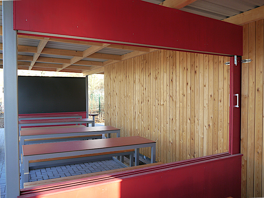 Blick durch roten Rahmen auf Tische, Bänke und Tafel