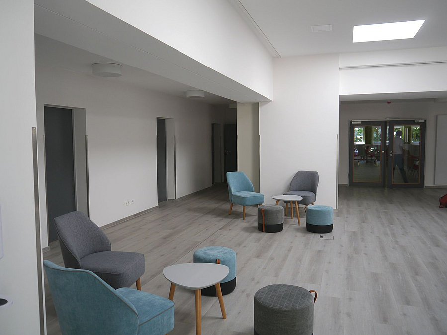 Raum mit hellem Fußboden und blau-grauen Sitzgruppen