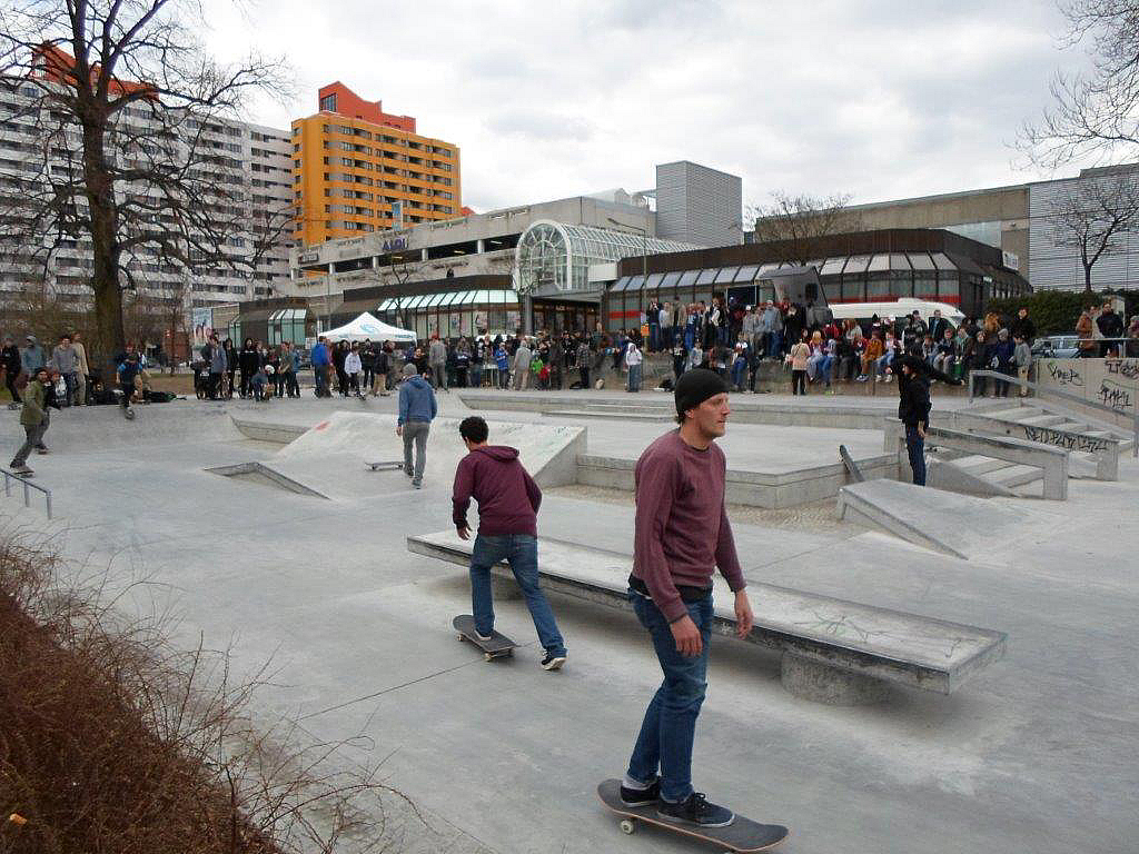 Skateboarder auf Betonpist vor Hochhäusern und Einkaufszentrum
