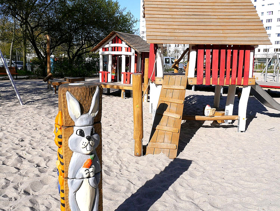 Hasenfigur an Holzpfosten, 2 Spielhäuser in rot und Weiß und Holzfarben