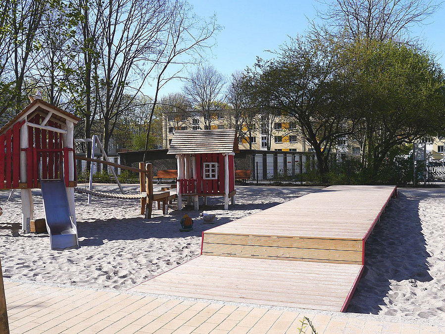Holzsteg mit Stufe, links Sandfläche mit Spielhäusern