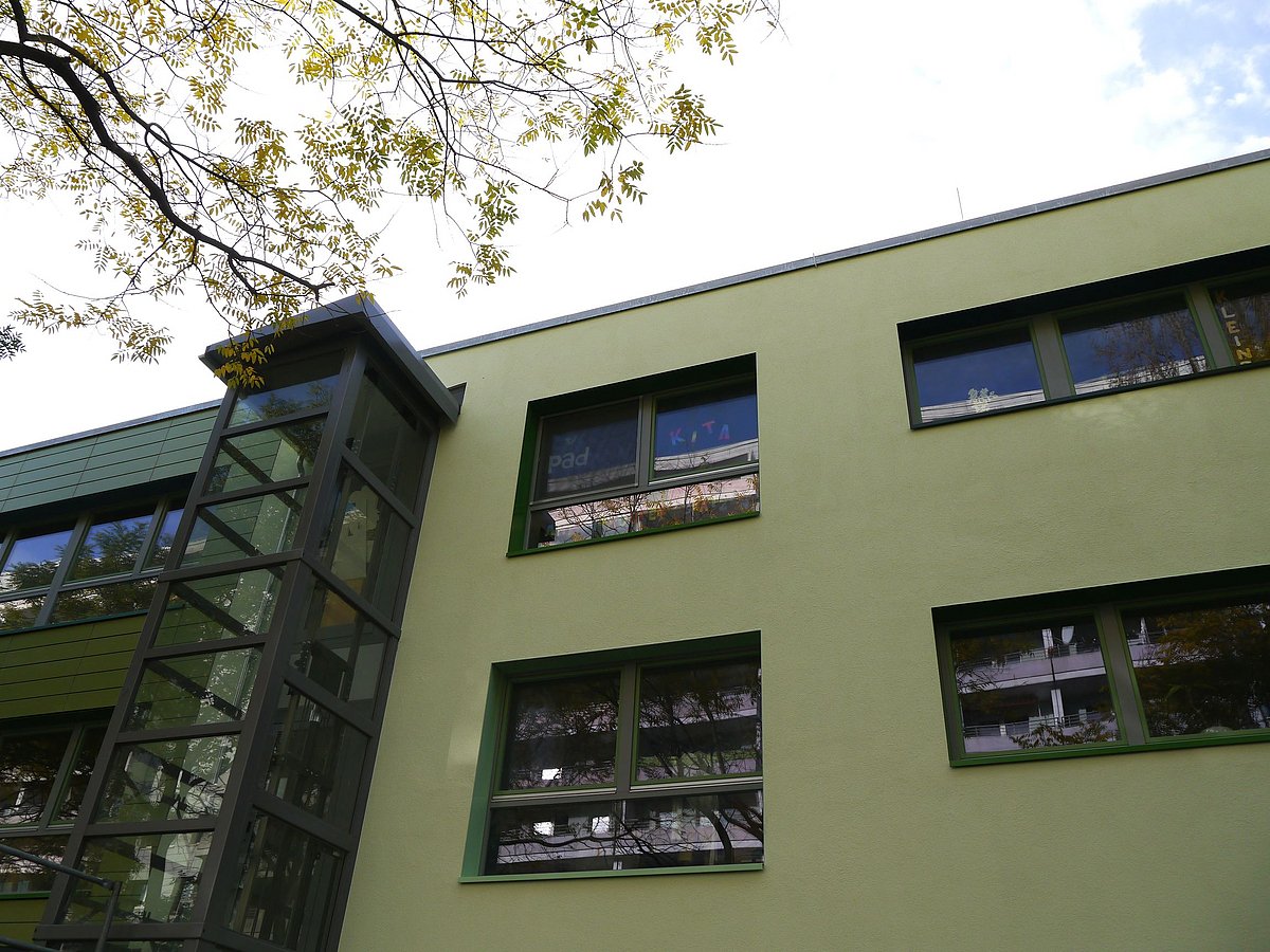 Detail einer hellgrünen Fassade mit gläsernem Aufzug