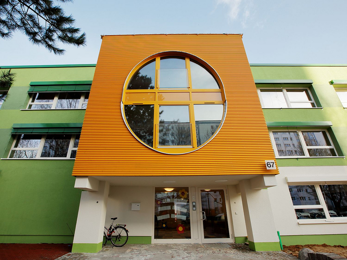 Eingang grüner Dreigeschosser mit vorgehängtem Erker in Orange mit ovalem Fensterausschnitt über zwei Etagen
