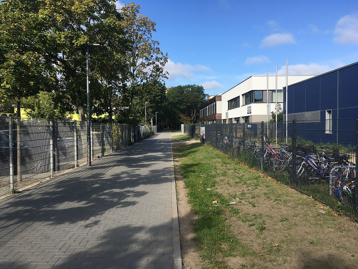 Pflasterweg neben eingezäunten Zweckbauten (Schule)