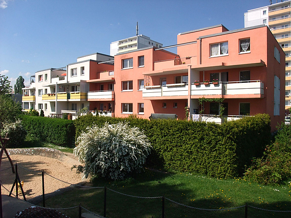 Dreigeschosser in rosa und weiß mit Dachgärten und Balkonen, davor Spielplatz