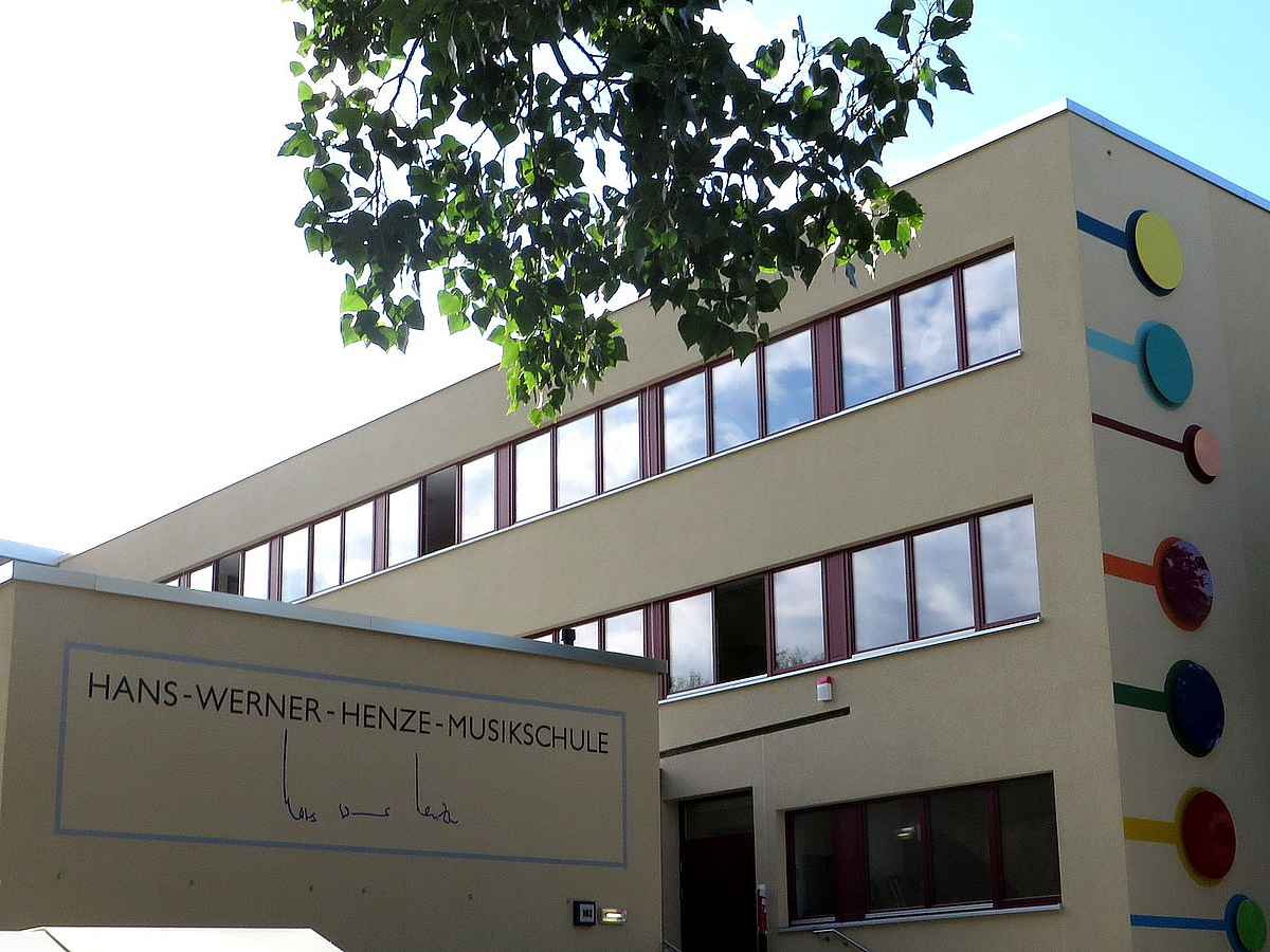 Plattenbauschule mit Vorbau, daran Unterschrift Hans Werner Henzes, am Hauptgebäude bunte, stilisierte Noten
