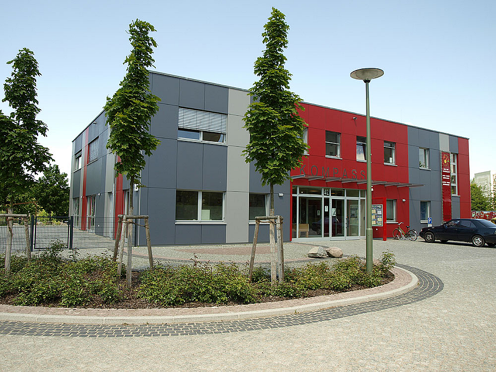 Modernes Gebäude in Rot und Grau mit Pflanzungen im Vordergrund