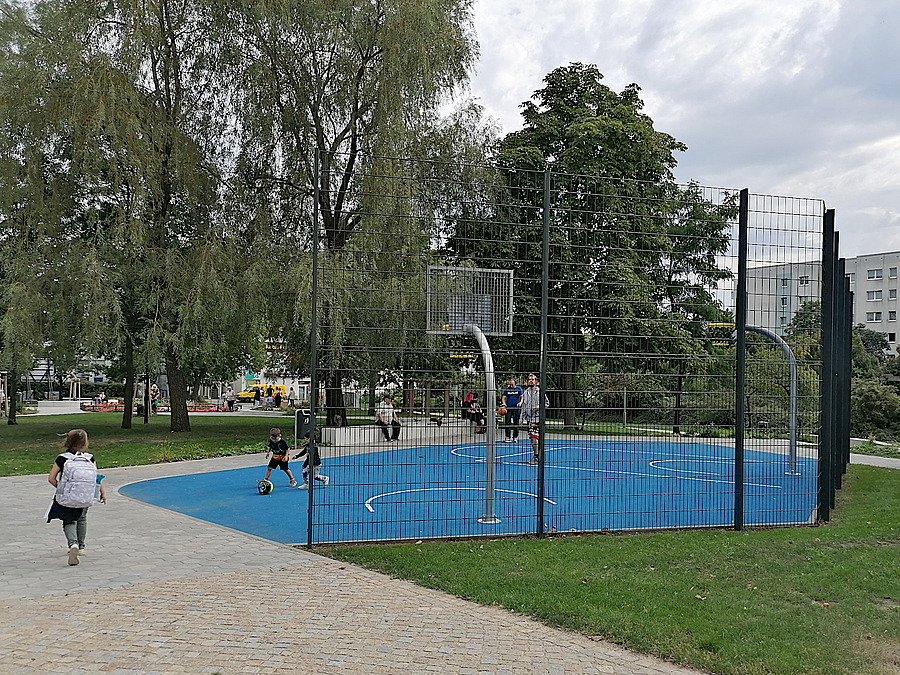 Basketballplatz mit Spielern auf blauem Boden, Rasen, Laubbäume