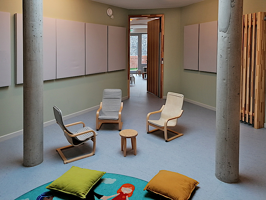 Raum mit Betonsäulen, 3 Kindersesseln und buntem Teppich mit Kissen