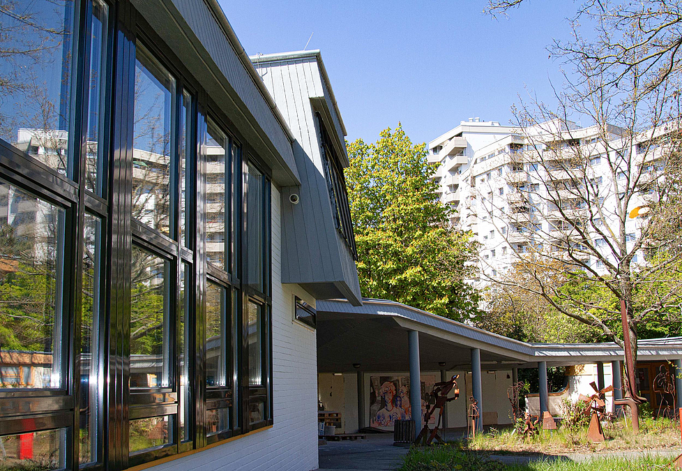 Blick entlang von Fenstern mit dunklen Metallrahmen auf ein langgezogenes Vordach auf Stützen