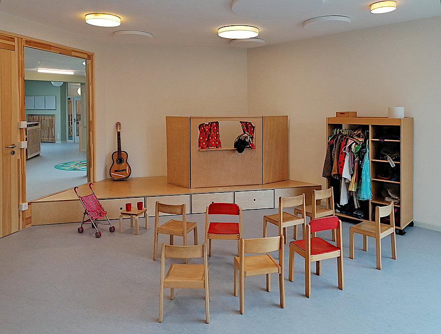 Raum mit Stuhlhalbkreis vor Puppenbühne, Tür und Fenster zum Gang