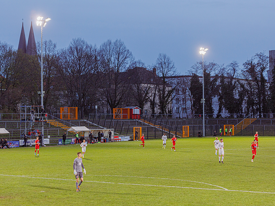 Fußballspiel unter Flutlicht, im Hintergrund Kirche