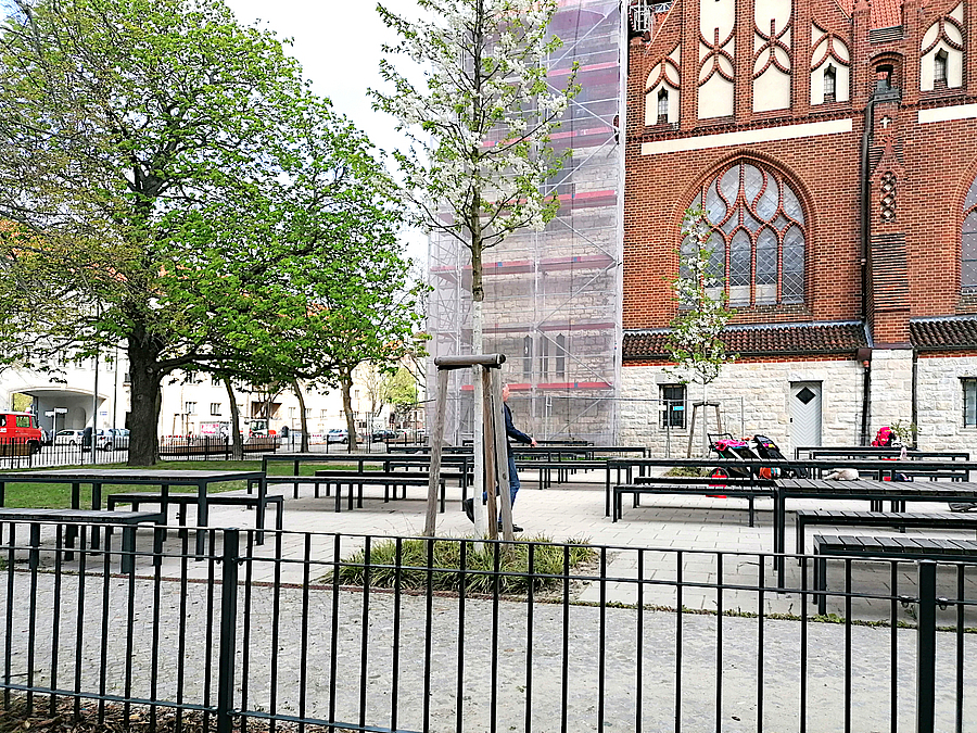 Tische und Bänke hinter niedrigem Zaun vor Kirche