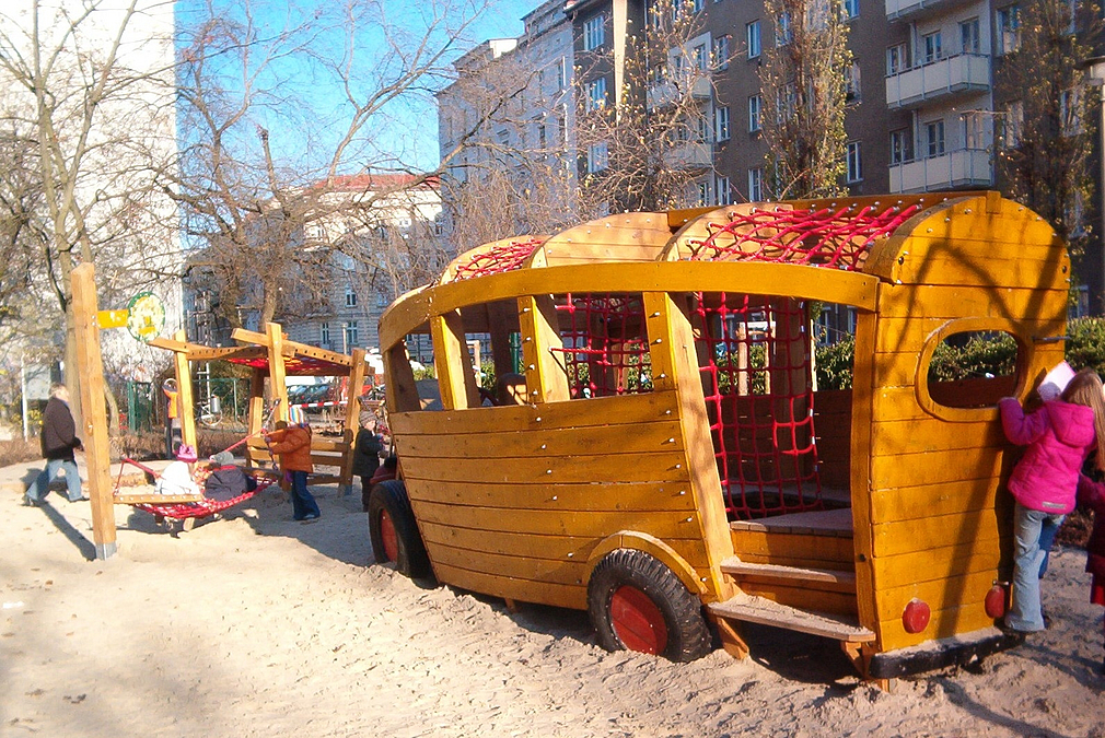 Spielbus aus Holz auf Sandfläche mit Kindern