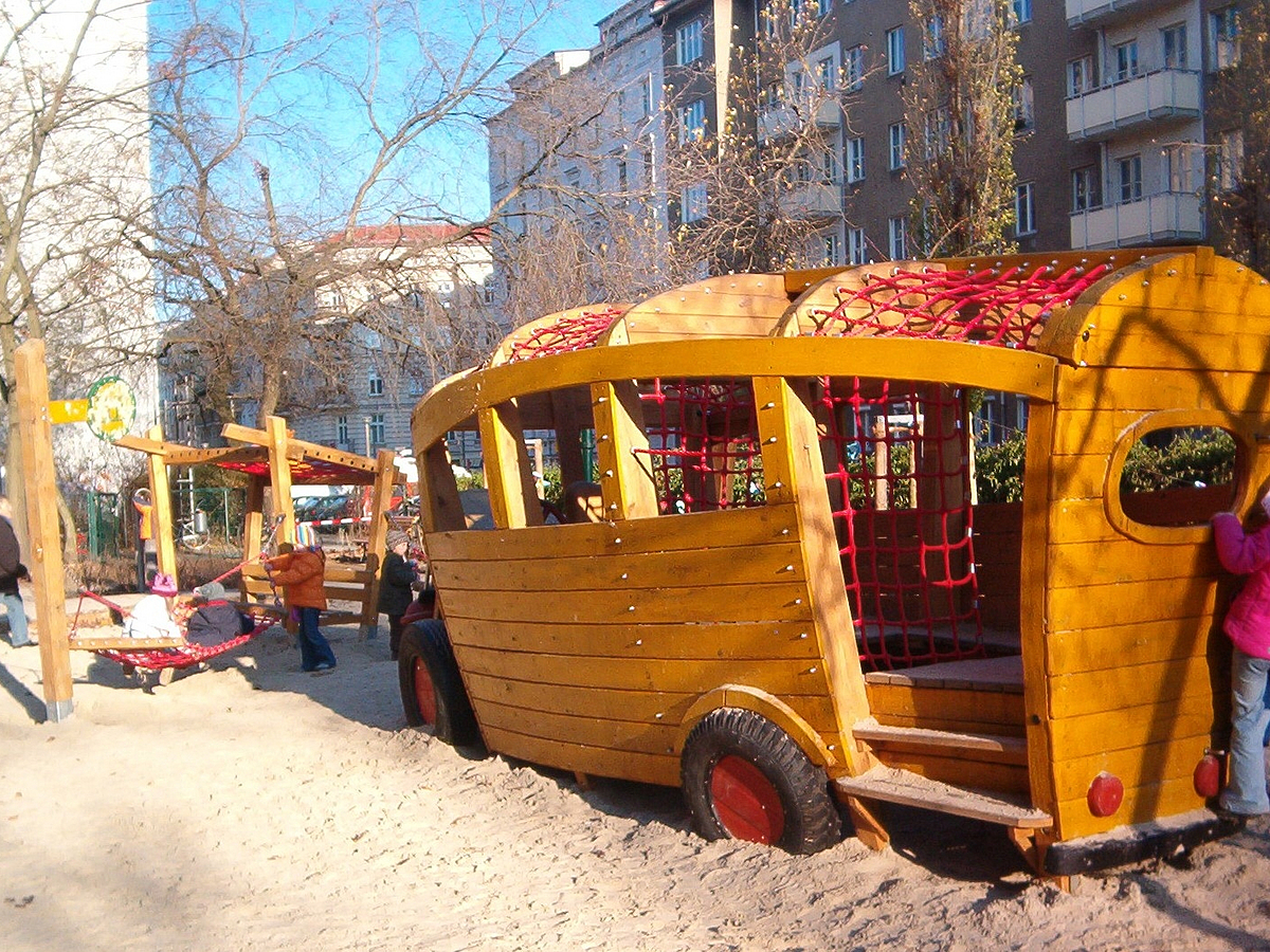 Spielbus aus Holz auf Sandfläche mit Kindern