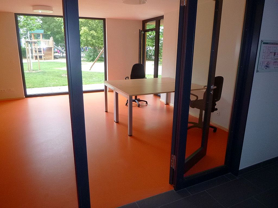 Durchblick vom Flur in Raum mit Schreibtisch und orangefarbenem Boden, bodentiefes Fenster zum Garten