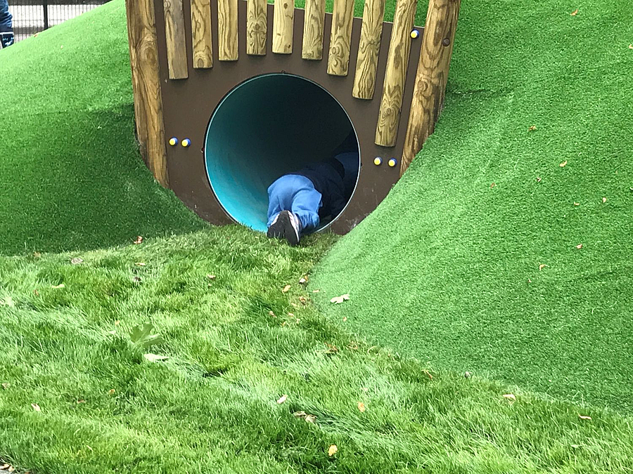 Kind kriecht in Tunnelröhre an grünem Hang