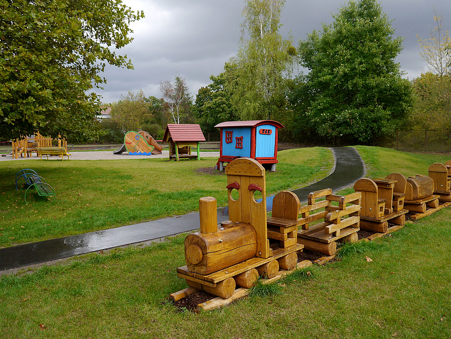 Holzeisenbahn auf Rasenfläche, Asphaltweg über Hügel