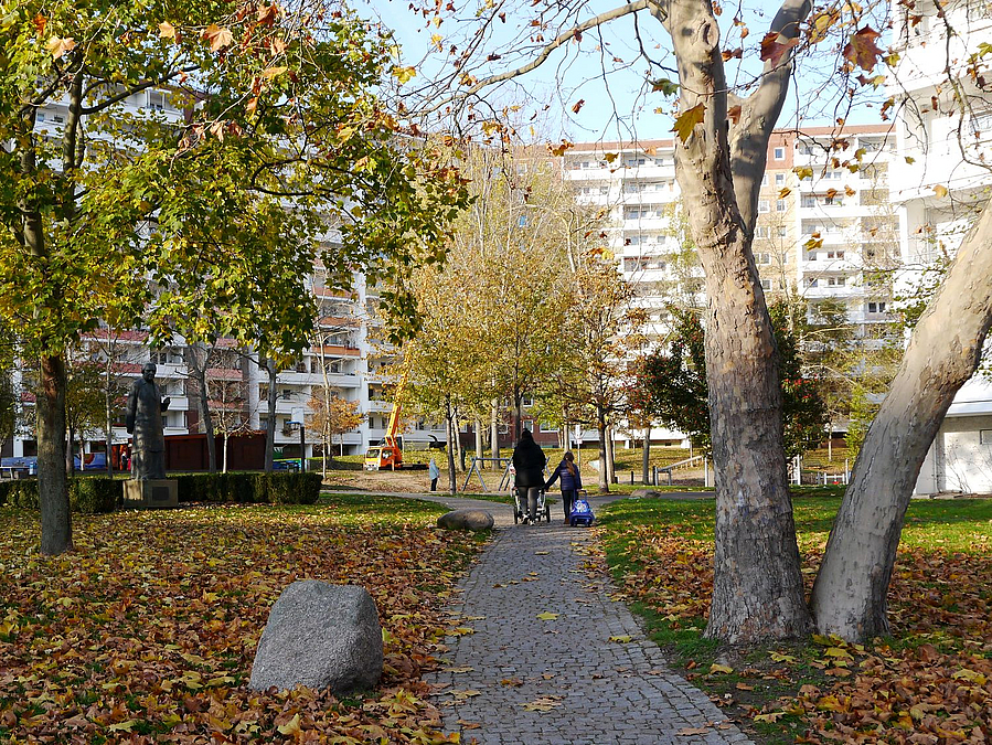 Herbstliche Grünanlage mit Fußweg und Findling, hinten steht quer ein Elfgeschosser