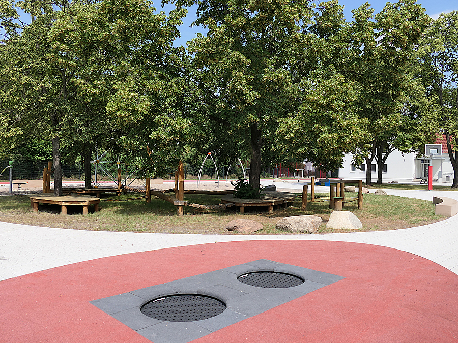 Platzfläche mit 2 eingelassenen Trampolinen, ovale Bauminsel mit Holzplattformen