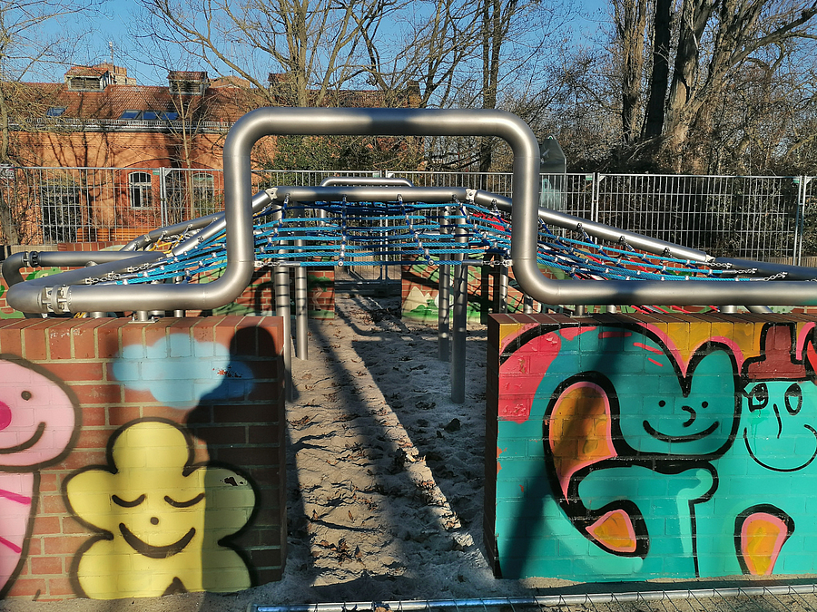 Klinkermauer mit buntem Graffiti, darüber Stahlgestgell mit Kletternetzen