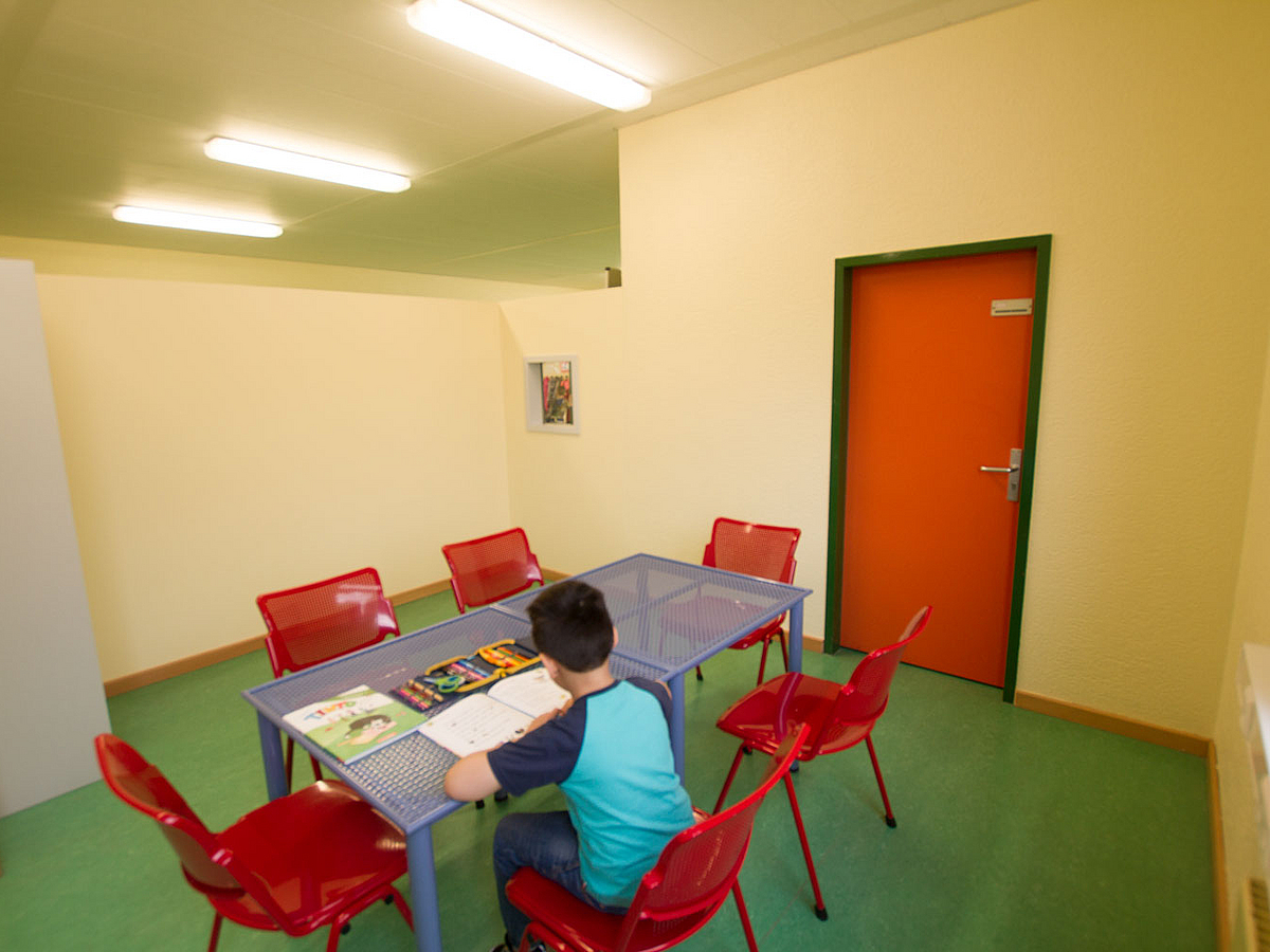 Kind am Tisch in Raum mit farbigen Wänden, Fußboden und Türen