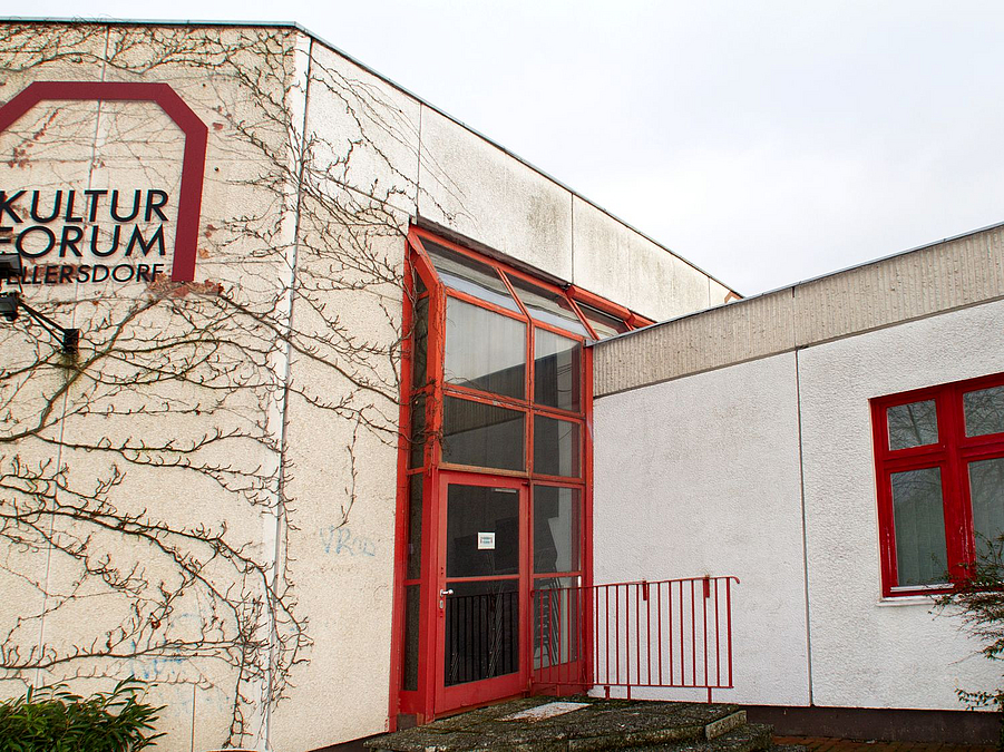 Ecke eines hellen Flachbaus mit roten Türen und Fenstern, Schriftzug Kulturforum