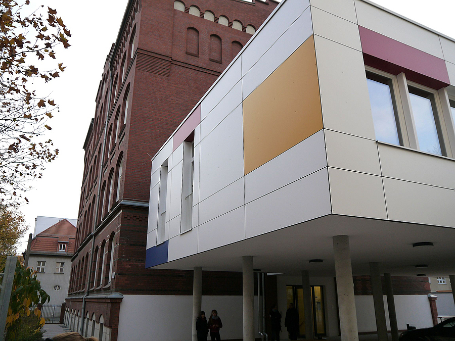 Moderner, heller Anbau mit Farbflächen an höherem Backsteingebäude
