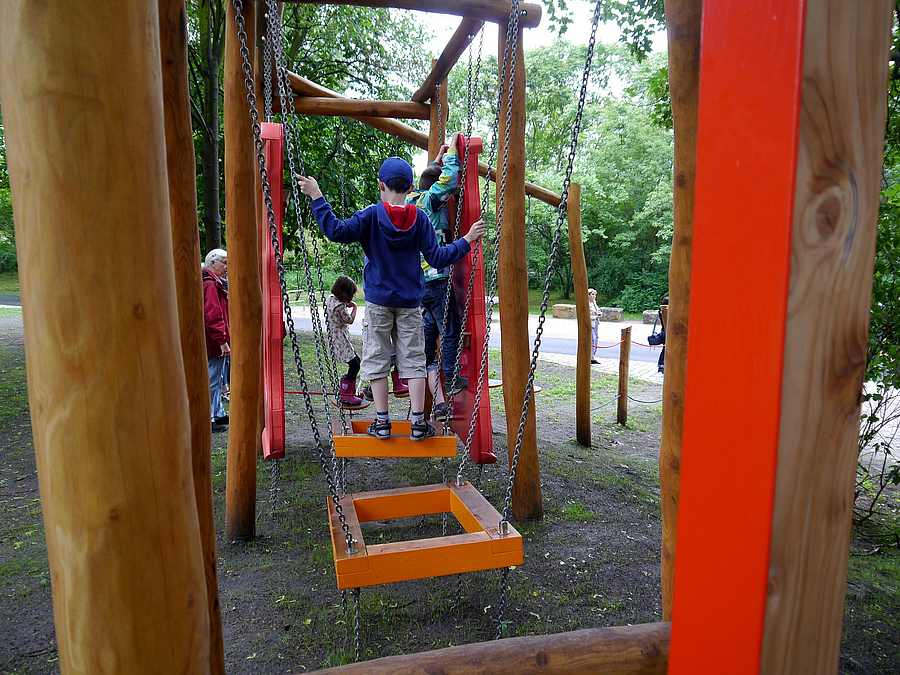 Kinder balancieren auf horizontal gelagerten Rahmen an Ketten - Rückansicht