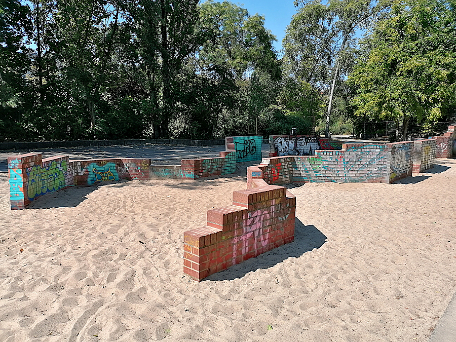 2 niedrige, abgestufte Klinkermauern mit Graffiti auf Sand