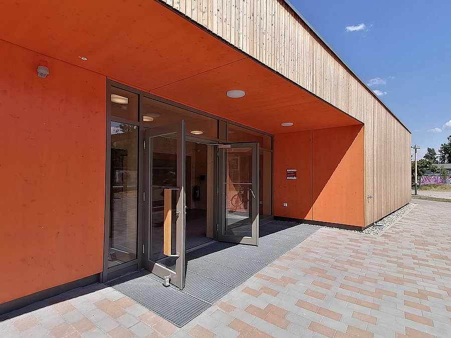 Eingang zurückgesetzt unter Holzlamellenfassade, orange gerahmt