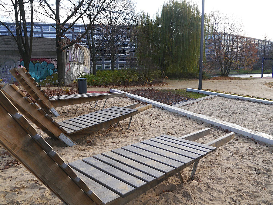 3 feste Liegestühle aus Holz auf Sandfläche, 2 gemauerte Terrassen