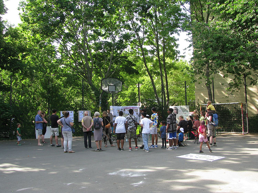 Menschen stehen auf Platz vor Bäumen - Rückansicht