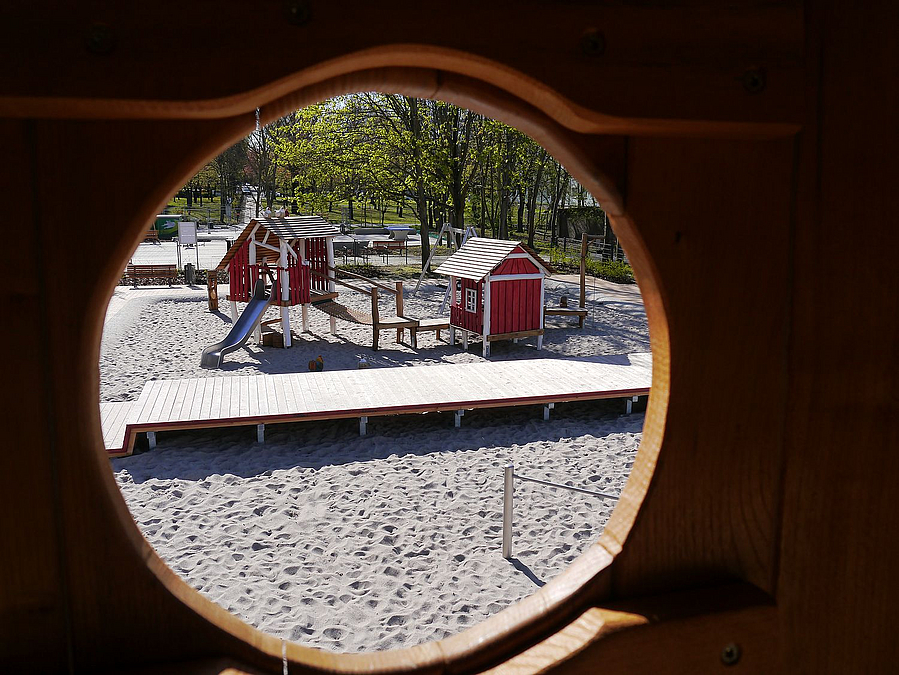 Blick durch runde Lück auf Holzsteg und Spielhäuser