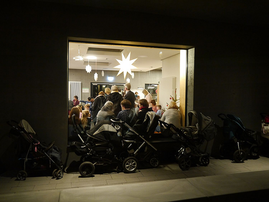 Blick durch Fensterfront in Raum mit vielen Menschen sowie leuchtenden Weihnachtssternen