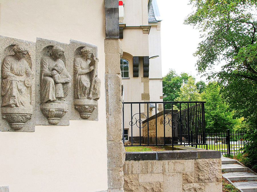 Figuren-Reliefs an heller Fassade, schmiedeeisernes Gitter