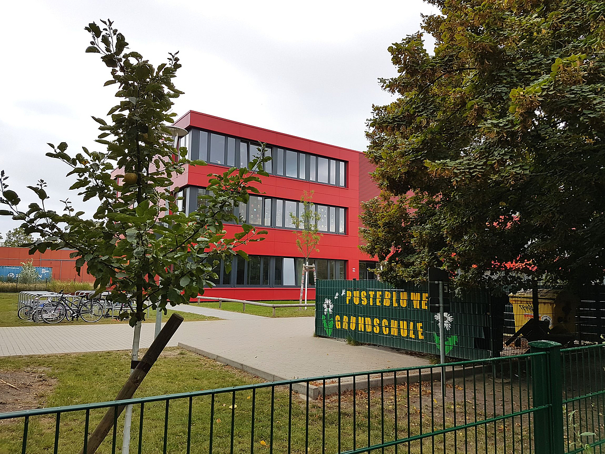 Roter Dreigeschosser, grüner Container mit SChriftzug Pusteblume-Grundschule, Laubbäume
