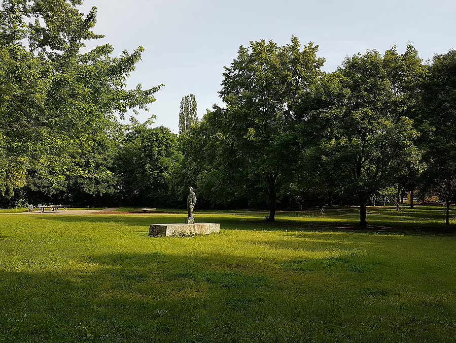 von Bäumen gerahmte Wiese mit Personendenkmal im Zentrum