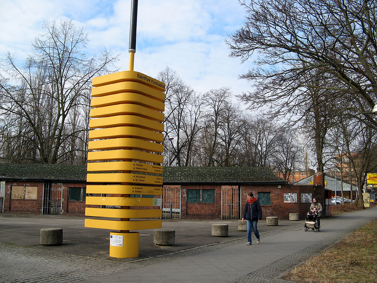 Gelbe Stele (siehe oben) auf kleinem Platz mit Kassenhäuschen aus Backstein