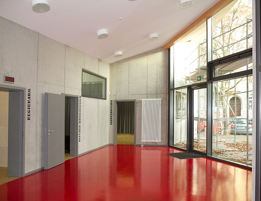 Glasfront zur Staße, roter Kunststoffboden, Eingänge zu verschiedenen Räumen gehen ab