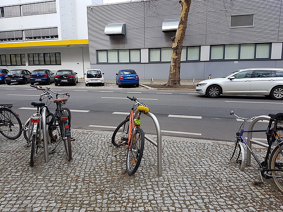 Straße mit Fahrradbügeln, auf der anderen Straßenseite Parkplätze