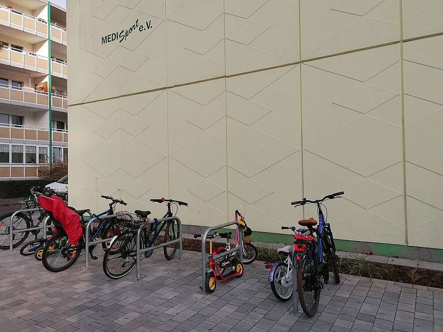 Hellgelbe Giebelwand mit Logo MEDI_Sport e. V., Fahrradbügel mit Kinderrädern 